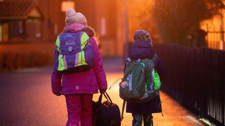 Zwei Schüler gehen am frühen Morgen auf dem Schulweg zu ihrer Grundschule. Künftig müssen sie auch bei Kontakt zu Infizierten nicht mehr in Quarantäne.
