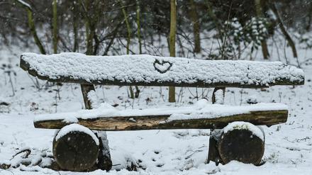 Eine Bank im Wald ist mit Schnee bedeckt. In den Schnee ist ein Herz gezeichnet. 