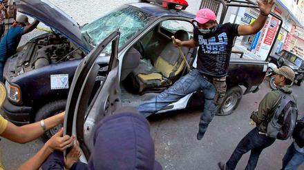 Wütende Demonstranten zerstören ein Polizeifahrzeug in Mexiko. Sie protestieren gegen den Tod linker Studenten im Auftrag von Politikern.