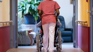 Eine Bewohnerin eines Pflegeheims wird von einer Pflegerin einen Gang entlanggeschoben.
