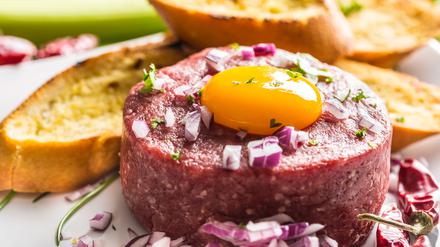Beef tartare with egg yolk red onion chili peppers herbs and bruschetta.