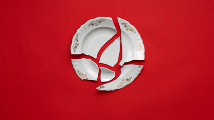 Zerbrochener Teller auf rotem Hintergrund als Symbol für häusliche Gewalt.