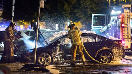Feuerwehrleute löschen ein brennendes Auto in der Weserstraße in Berlin-Friedrichshain. 