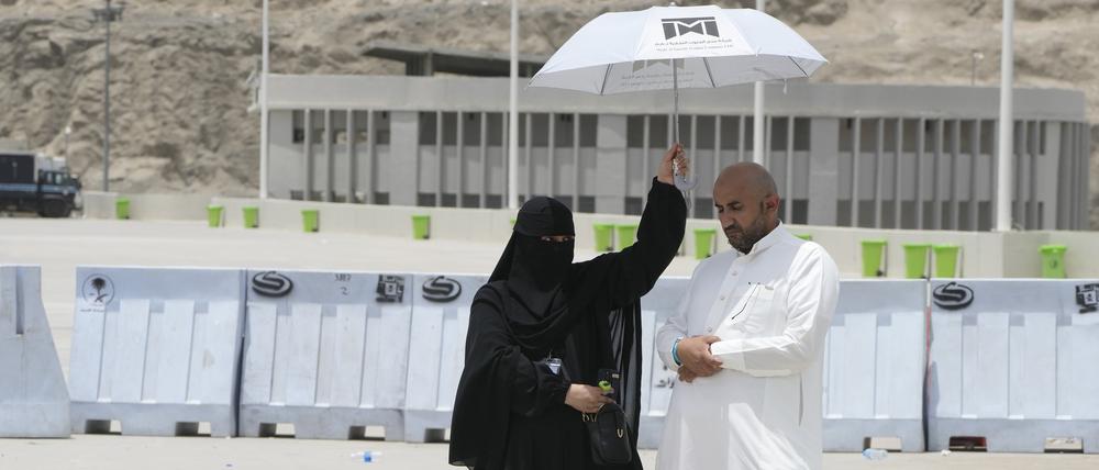 Eine Frau hält einen Schirm über einen Mann, der sein Gebet am letzten Tag der Hadsch in Mekka iN Saudi-Arabien verrichtet.