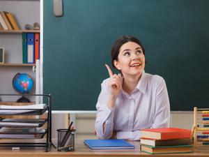 Eine junge Lehrerin sitzt in einem Klassenzimmer. (Symbolbild)
