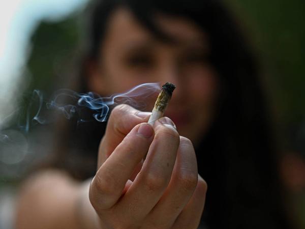 Eine junge Frau hält bei einer Pro-Cannabis-Demo einen Joint in die Kamera.