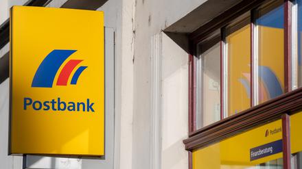 Ein Schild mit dem Logo der Postbank ist an der Fassade einer Bankfiliale angebracht. 