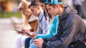 Group of teenagers sitting outdoors using their mobile phones