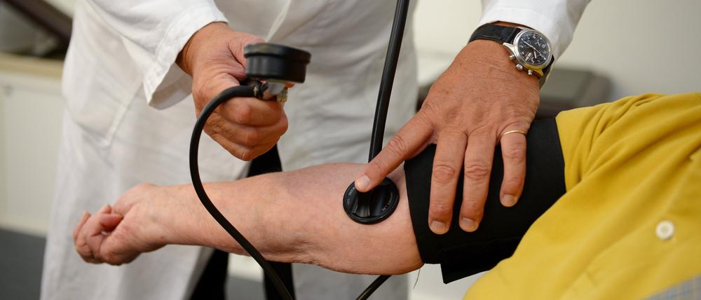 Ein Hausarzt misst in seiner Praxis einer Patientin den Blutdruck.  