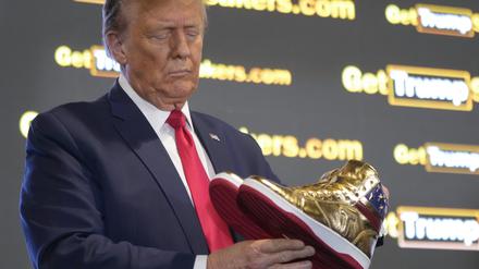 Der republikanische Präsidentschaftskandidat und ehemalige Präsident Donald Trump hält goldene Trump-Sneakers auf der Sneaker Con Philadelphia, einer Veranstaltung für Sneakersammler, in Händen. 