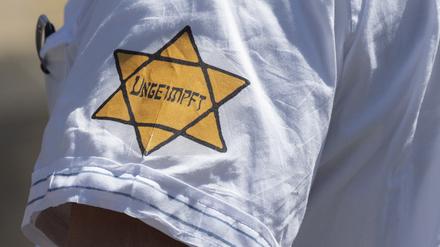 "Ungeimpft" steht auf einem nachgebildeten "Judenstern" am Arm eines Mannes auf einer Demonstration.