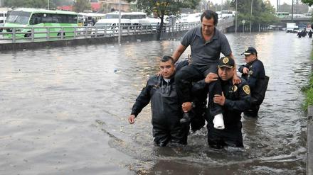 Polizisten tragen einen Mann nach einem Unwetter durch eine überschwemmte Straße in Mexiko-Stadt. Für Mega-Städte ist es besonders schwer, sich an den Klimawandel anzupassen. 