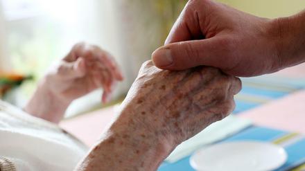 Ein Pfleger hält in einem Alten-und Pflegeheim die Hand einer Bewohnerin.