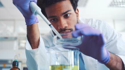 Ein junger Wissenschaftler hantiert im Labor mit Pipette und Petrischale.